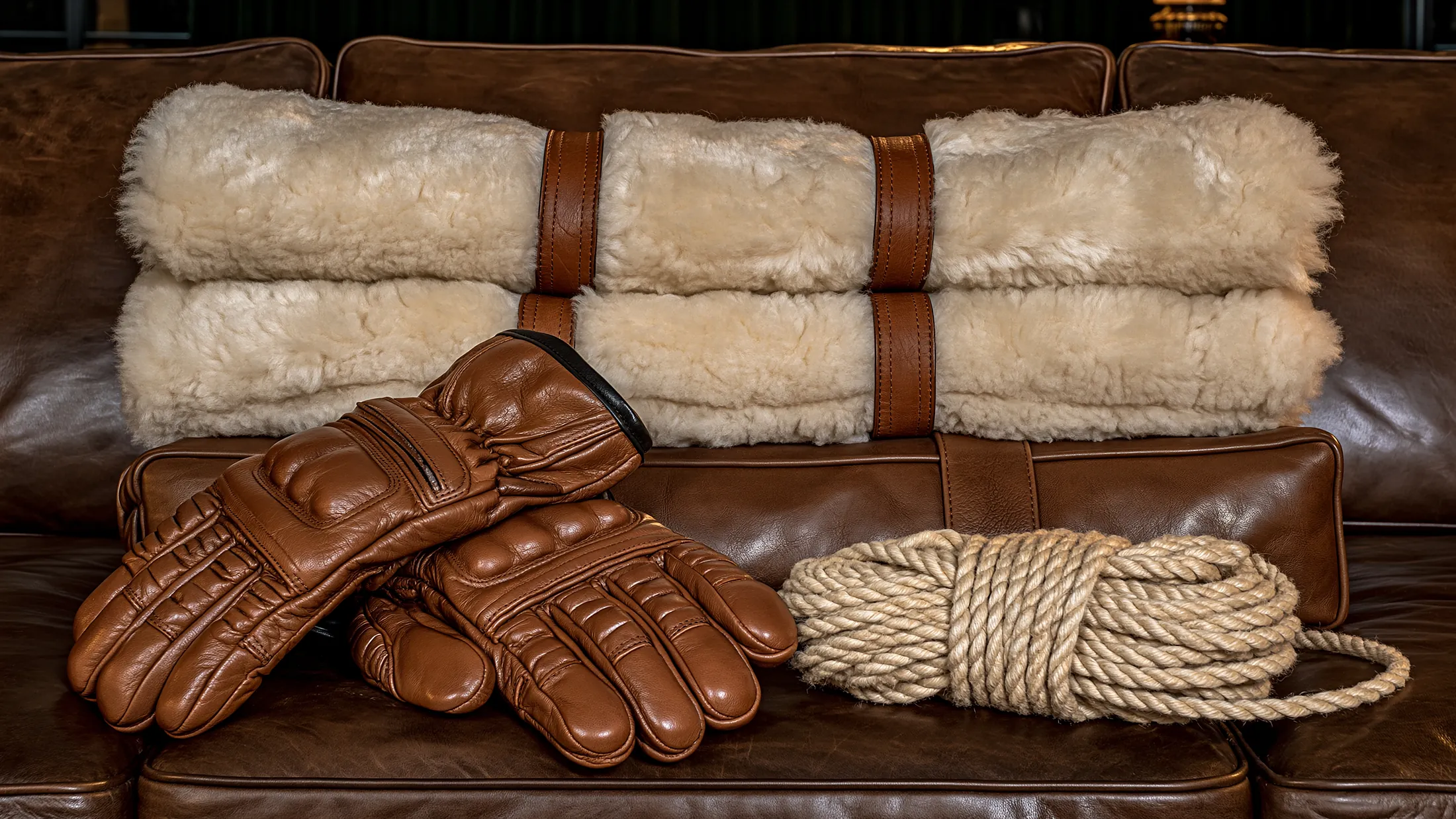 Des tubes doublés de mouton, une paire de gants de cuir brun et une corde de coton enroulée, sur un canapé de cuir.